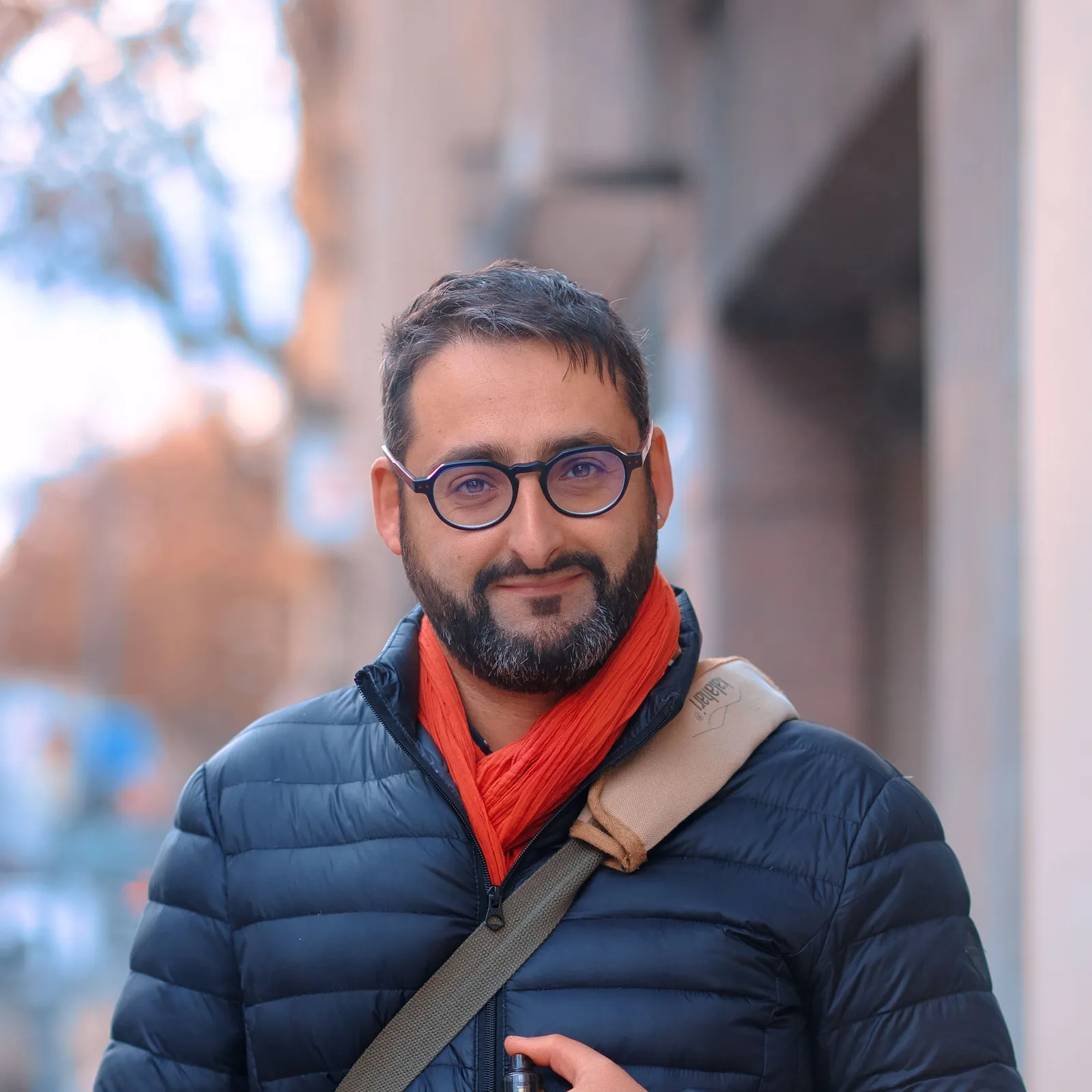 Un homme à lunettes et écharpe rouge sourit dans une rue de ville